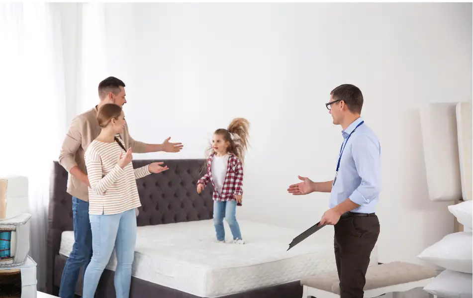 a girl jumping on the mattress while her parents and a salesman try to stop her