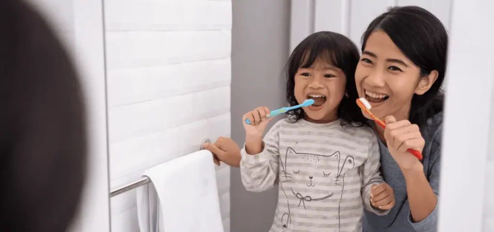mom showing her kid the proper way to brush her teeth