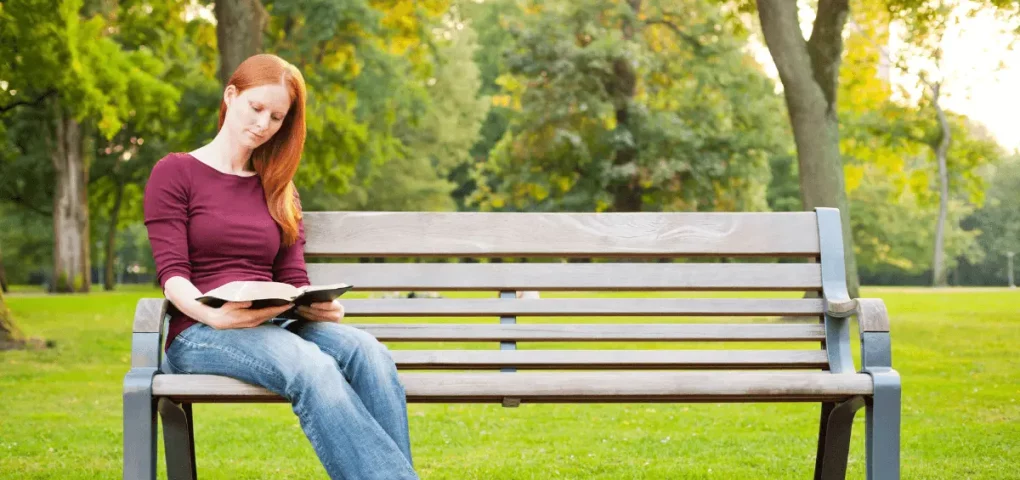 woman reading the bible while sitting on the bench